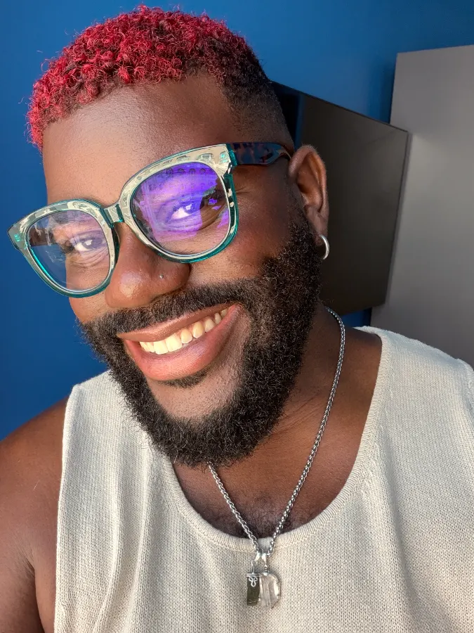 Victor laughing against a blue wall, his short curls colored a bright red