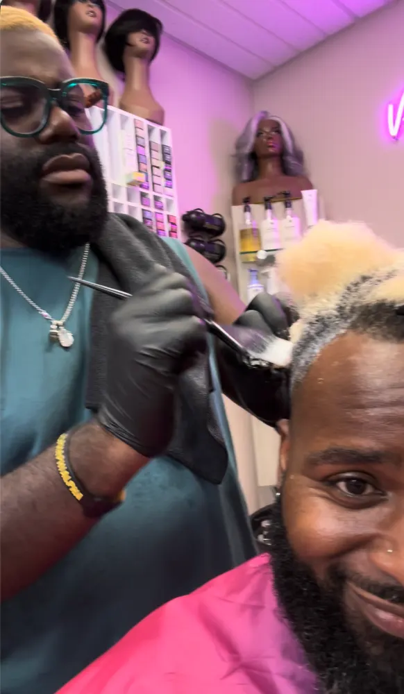 Victor in gloves brushing color onto a smiling guest's lightened short hair