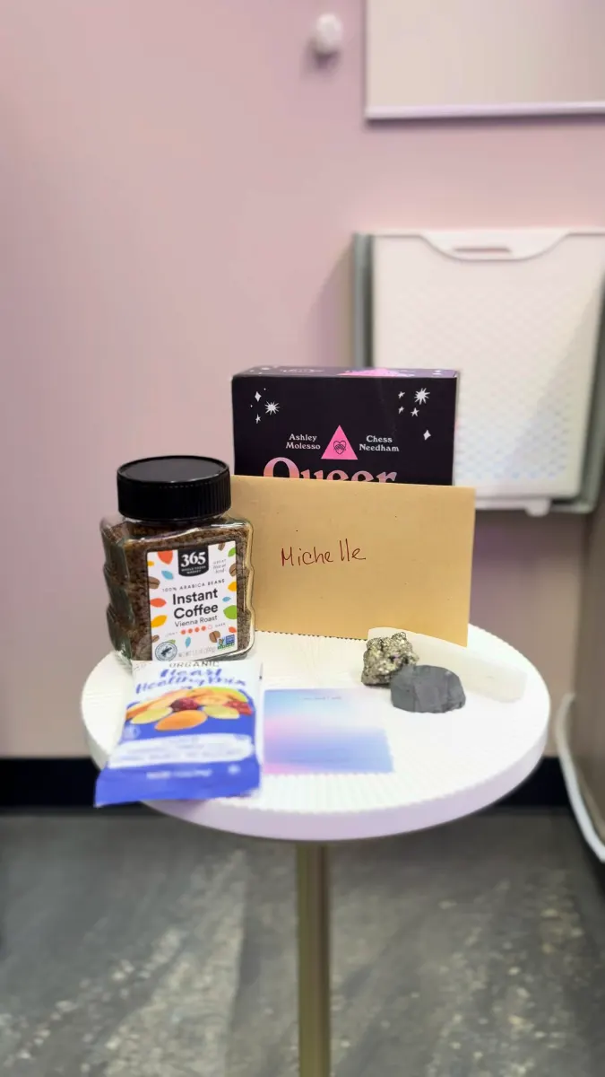 A small round side table set for a guest: a tarot deck, a handwritten envelope with their name, instant coffee, a trail-mix snack, a notepad and three crystals